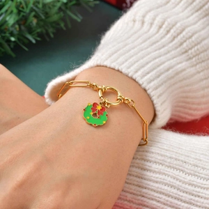 Détail d'un bracelet doré avec pendentif couronne de Noël sur fond de pull en maille blanc