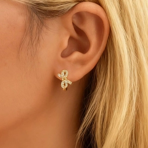 Gros plan d'élégantes boucles d'oreilles nœuds dorées serties de zircons sur l'oreille