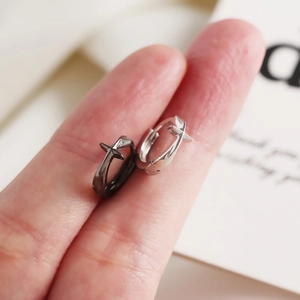 Gros plan de créoles minimalistes en argent S925 avec croix en finitions noir et argent