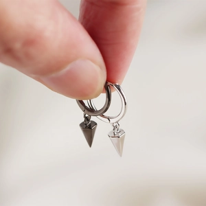 Detail of silver and black punk cone hoop earrings held in hand to show size