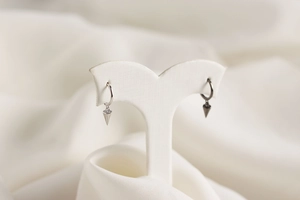 Macro shot of S925 sterling silver hoop earrings with geometric cone charms on white silk