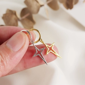 Detail of gold and silver star charm hoop earrings held in hand for scale and texture