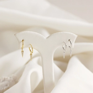Detail view of gold and silver triangle drop earrings with cubic zirconia on white stands