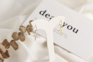 Close-up of minimalist gold and silver star earrings on a white jewelry display stand
