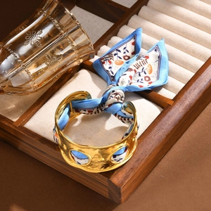 Goldener hohler Armreif mit blauem Seidentuch auf einem hölzernen Schmucktablett