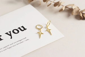 Detailed close-up of gold star hoop earrings on a decorative greeting card background