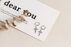 Detail of S925 sterling silver hoop earrings with four-pointed star pendants