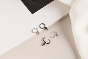 Detail of silver and black geometric spike drop hoop earrings on a soft satin fabric background