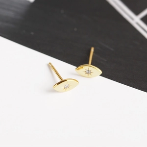 Macro detail of gold eye-shaped stud earrings with starburst engraving and small zircon