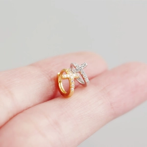 Macro shot of silver and gold cross hoop earrings with crystals on a fingertip