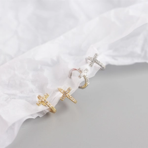 Macro shot of silver and gold cross hoop earrings with inlaid zircon on white paper