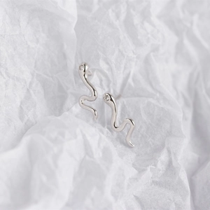 Macro shot of silver snake stud earrings with clear zircon on a white textured background