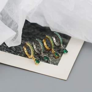 Close-up of gold and silver hoop earrings with green pear-shaped drop crystals