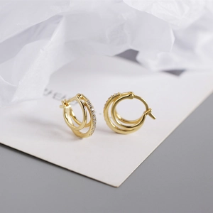 Gros plan de boucles d'oreilles huggie triples dorées avec une bande sertie de zircons