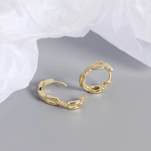 Macro detail of gold hoop earrings featuring textured chain links and paved zircons