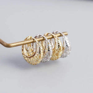 Detail view of hollow geometric patterned hoop earrings in gold and silver finish