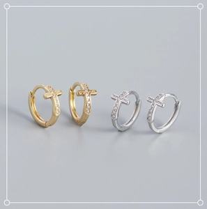 Close-up of gold and silver cross hoop earrings with inlaid clear zircon stones