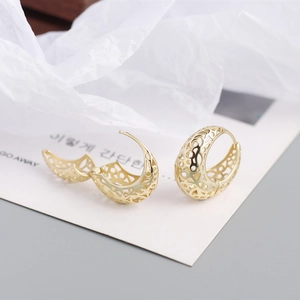 Detail of C-shaped hollow gold earrings with intricate patterns on a white card