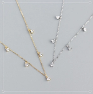 Dettaglio ravvicinato di collane S925 in oro e argento con ciondoli in zircone su sfondo grigio