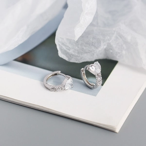 Macro shot of S925 silver heart hoop earrings with sparkling cubic zirconia on paper