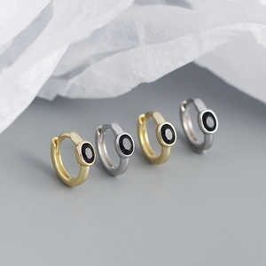 Detailed view of silver and gold oval black zircon hoop earrings on textured paper