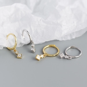 Close-up of geometric square drop earrings in gold and silver with zircon stones