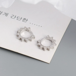 Macro shot of silver geometric huggie earrings with sparkling pavé zircons and sunburst edge