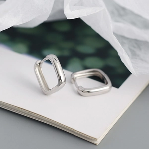 Gros plan détaillé de boucles d'oreilles créoles rectangulaires en argent sur fond blanc pur