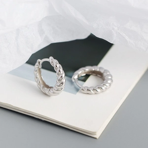 Détail de boucles d'oreilles créoles torsadées en argent S925 sur fond blanc minimaliste