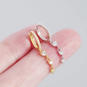 Gros plan de boucles d'oreilles pendantes en or et argent avec zircons sur les doigts
