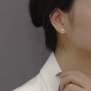 Close-up van geometrische gevlochten vierkante oorknopjes met een gouden afwerking