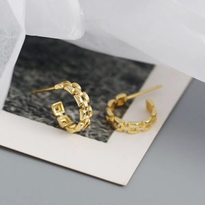 Macro shot of gold geometric hollow C-shaped earrings with watch strap chain texture