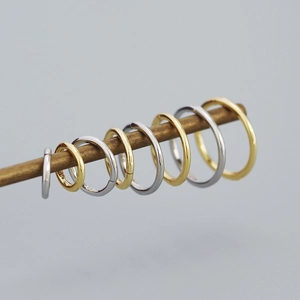 Detailed view of gold and silver S925 sterling silver hoop earrings on a brass display rod