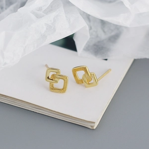 Detail van geometrische in elkaar grijpende gouden vierkante oorbellen met textuurafwerking