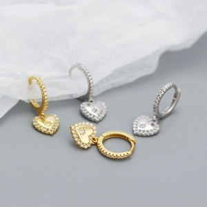 Macro shot of silver and gold heart huggie earrings with sparkling starburst engravings