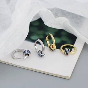 Detail of silver and gold huggie earrings with spinning blue zircon beads on grey surface