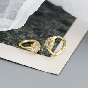 Détail de boucles d'oreilles fleur dorées avec zircons blancs sur fond neutre