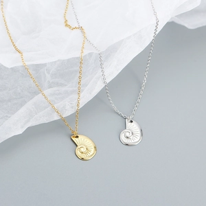 Detailed view of gold and silver nautilus shell necklaces with radial texture on a grey-blue surface