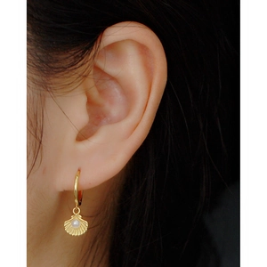 Close-up of a gold shell earring with a pearl on a model, highlighting high-end marine style
