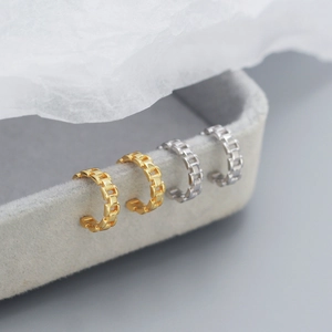 Detailed view of silver and gold chain-link ear cuffs on a soft velvet display stand