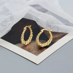 Detailed close-up of S925 silver stamp on twisted gold hoop earrings with cubic zirconia