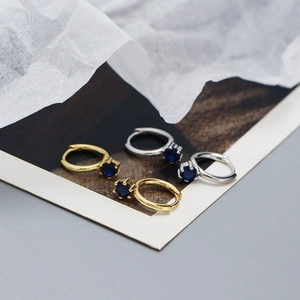 Close-up of gold and silver hoop earrings featuring six-prong set deep blue stones