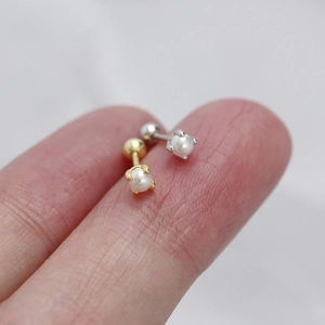 Detailed macro view of mini pearl labret earrings in gold and silver on a fingertip