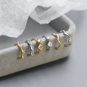 Close-up of gold and silver ear bone clips with zircon stones on a gray jewelry box