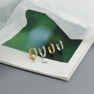 Detailed view of gold and silver S925 sterling silver 7mm hoop earrings on a magazine