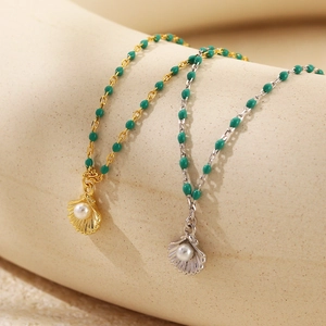 Dettaglio di ciondoli con perla a conchiglia e catena verde in finitura oro e argento