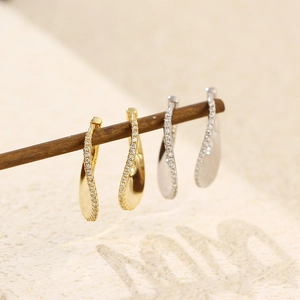 Dettaglio di orecchini a U con pavé di zirconi in oro e argento appesi su un legno
