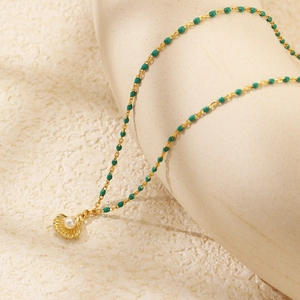 Dettaglio di una collana a conchiglia dorata con perla bianca e perline verdi su pietra fine