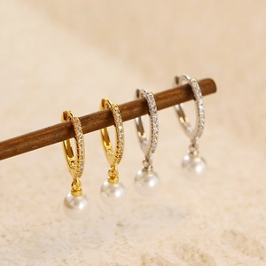 Détail de boucles d'oreilles perles argent et or avec zircons sertis sur support bois