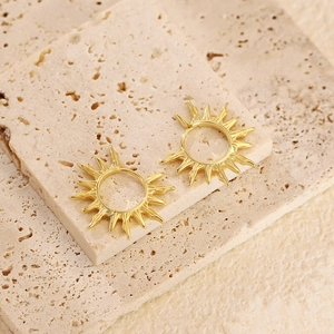 Détail macro de créoles dorées au motif soleil posées sur une surface en pierre beige